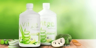 Two bottles of aloe vera health drink with aloe and fruit slices against a green background.